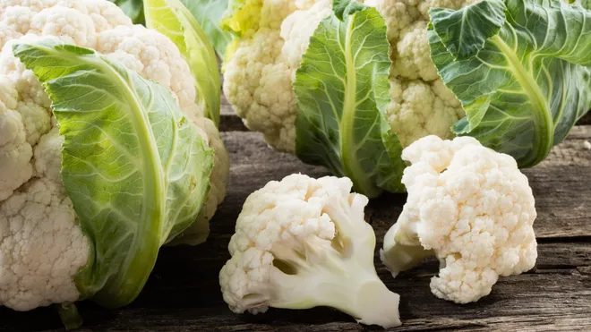 Freshly harvested cauliflower heads and florets placed on a rustic wooden table